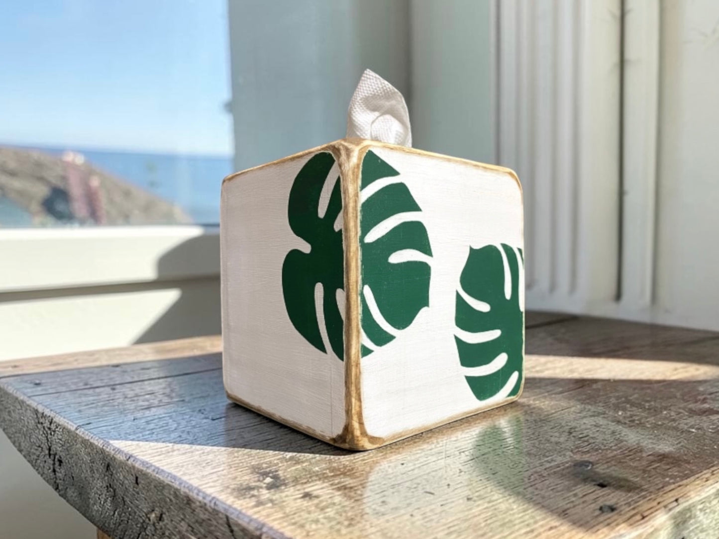 Monstera leaf tissue box cover for coastal bathroom decor and tropical beach house interiors, featuring a hand-distressed weathered finish inspired by tropical foliage, relaxed seaside living, and breezy coastal style. Designed for spa bathrooms, guest rooms, beach cottages, and light-filled coastal interiors.