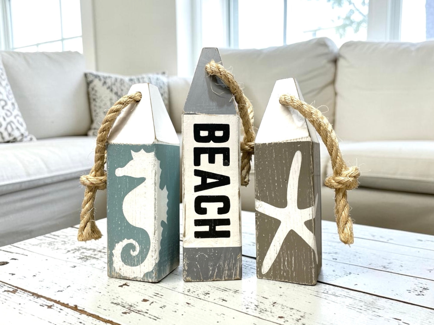 Decorative beach wood buoy set featuring hand-painted seahorse and starfish details with a distressed nautical finish. Coastal home decor for beach houses, coastal cottages, beach-themed rooms, ocean-inspired spaces, and seaside homes