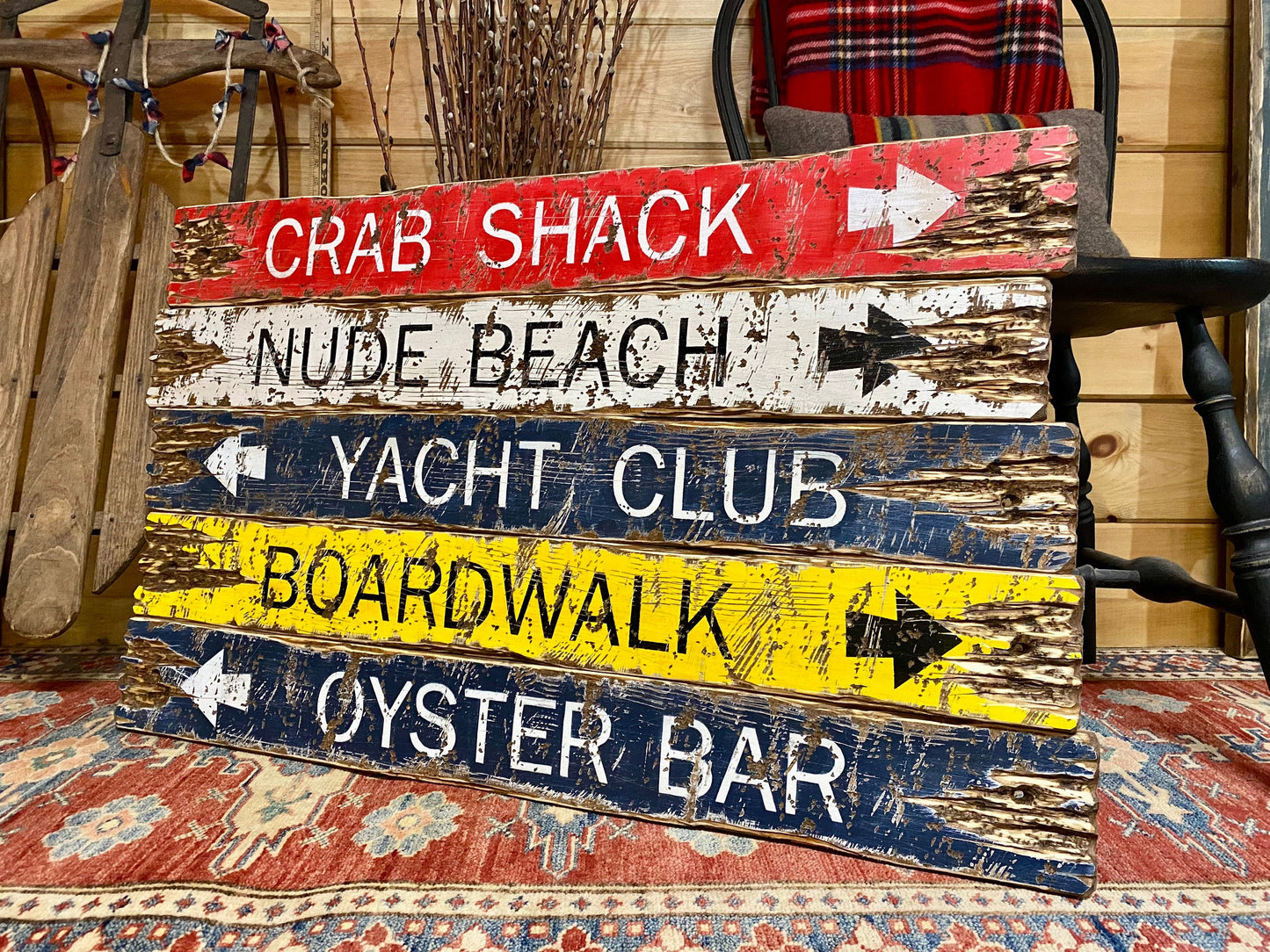 Hand-painted coastal beach sign in red, white, blue, and yellow with arrows for Crab Shack, Nude Beach, Yacht Club, Boardwalk, and Oyster Bar, rustic nautical wall art for seaside cottages