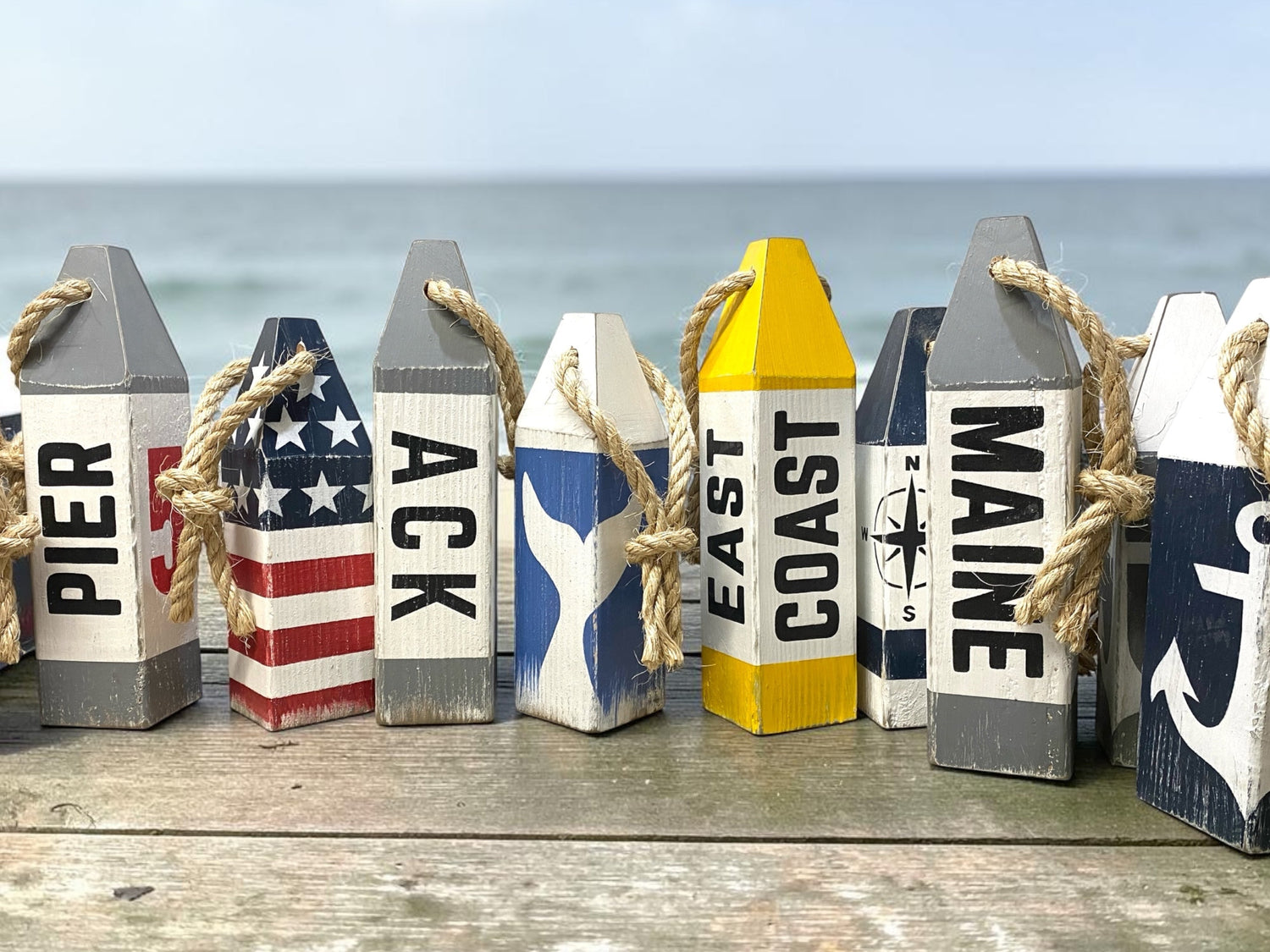 Decorative wood buoys displayed by the ocean featuring hand painted nautical & coastal themes. Rustic painted buoys for beach homes, coastal cottages, nautical spaces, beach themed rooms and great for boating gifts. New England style decor