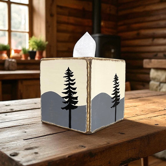 Rustic wooden tissue box cover with hand-painted mountain and pine tree design, camp cabin lodge décor on wooden table.