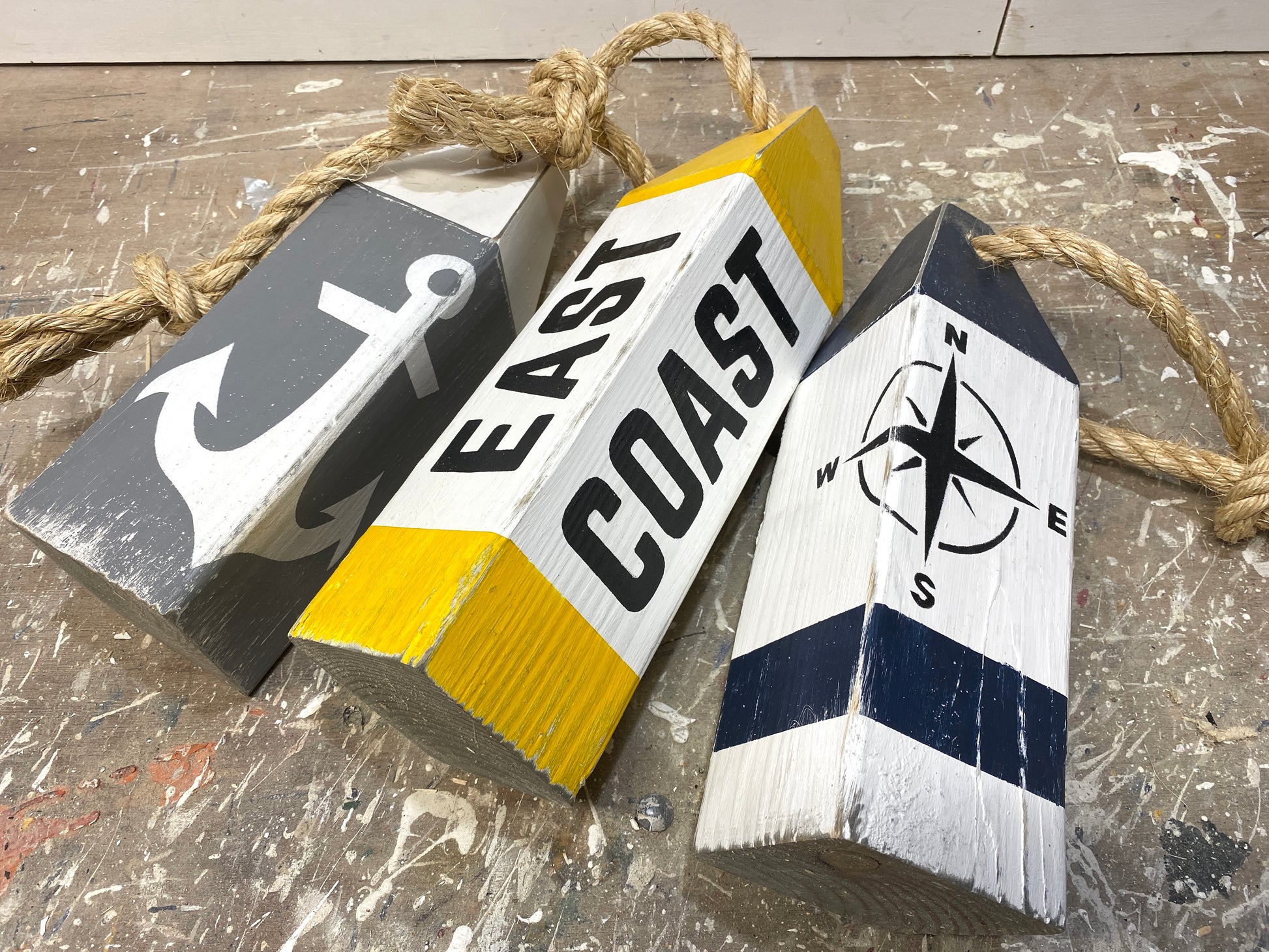 Close-up of decorative East Coast nautical buoy showing hand-painted compass rose and anchor details, distressed wood texture, and rustic coastal decor style