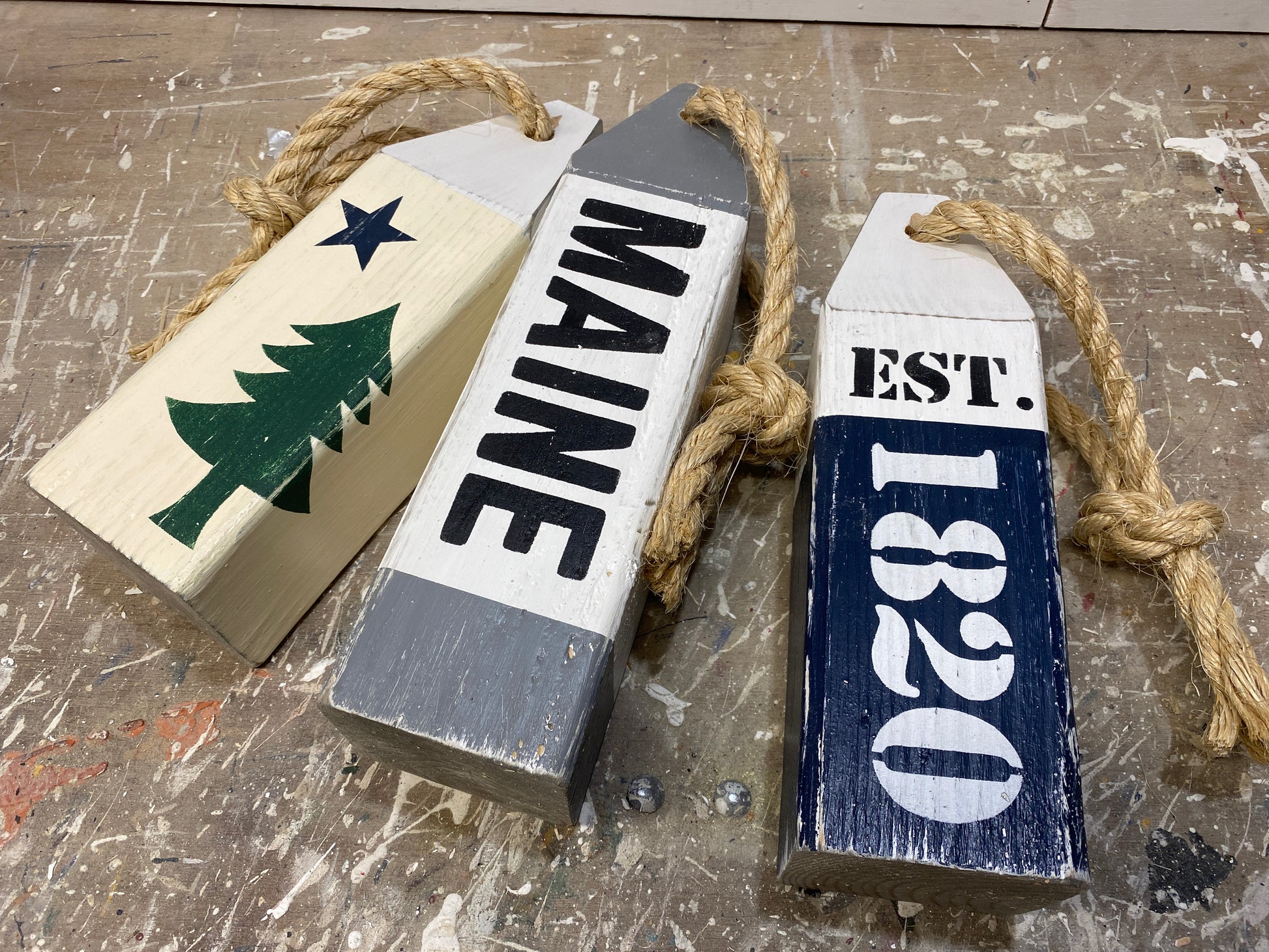 Close-up of decorative Maine nautical wood buoy featuring hand-painted original Maine flag design, established date details, distressed finish, and rustic coastal decor style. Perfect for beach houses, coastal cottages, seaside rooms, and New England homes.