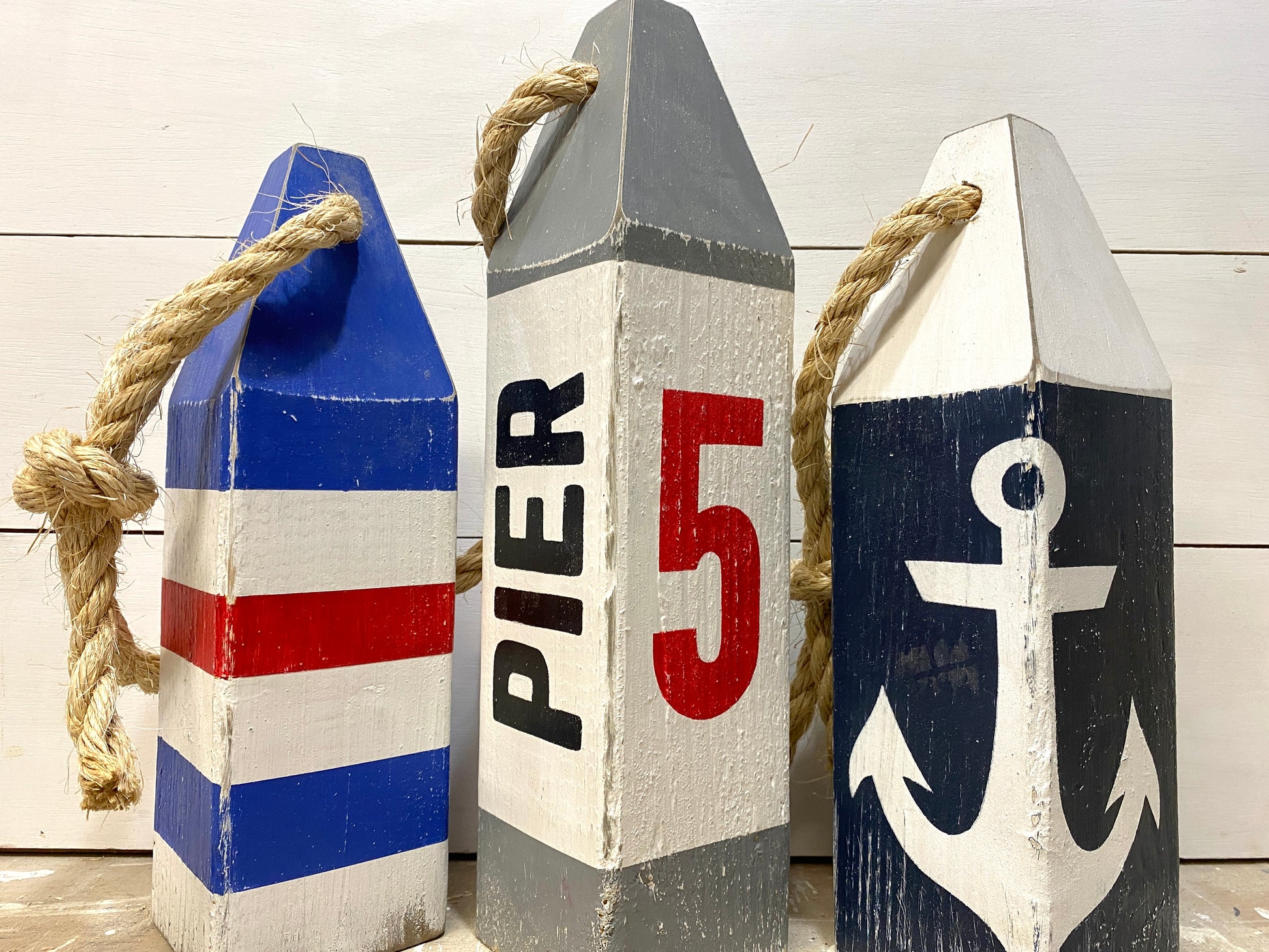 Close-up of a hand-painted Pier 5 nautical lobster wood buoy showing distressed wood texture, coastal colors, and rustic nautical details. Handmade coastal decor inspired by New England harbors, boating, sailing, beach houses, and waterfront living.