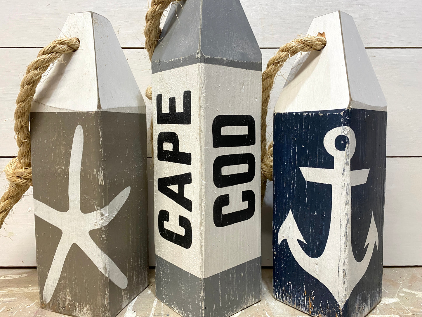 Close-up of Cape Cod nautical buoys showing hand-painted starfish and anchor details, rustic wood texture, and coastal decor style. Perfect for beach house decor, cottage decor, nautical rooms, and seaside spaces.