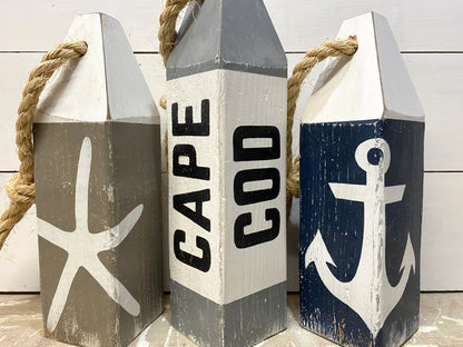 Close-up of Cape Cod nautical buoys showing hand-painted starfish and anchor details, rustic wood texture, and coastal decor style. Perfect for beach house decor, cottage decor, nautical rooms, and seaside spaces.
