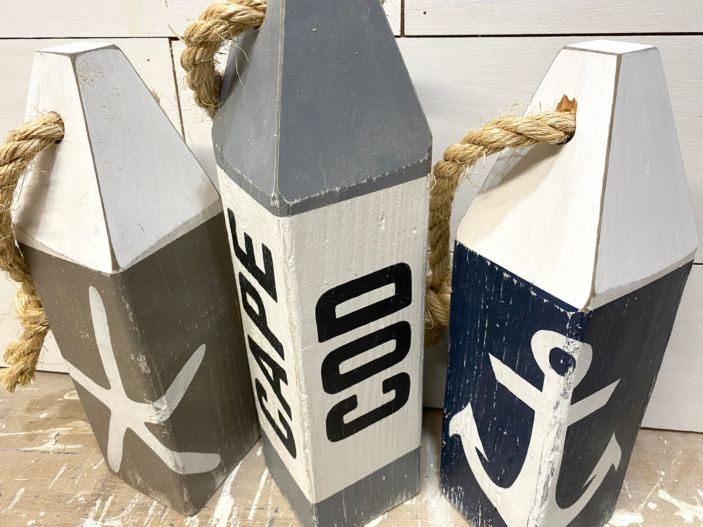 Close-up of Cape Cod wood buoy set featuring hand-painted starfish and anchor designs, distressed wood finish, and rustic nautical details. Coastal decor for beach houses, coastal cottages, beach-themed rooms, nautical spaces, and seaside homes