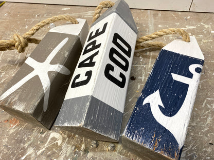 Close-up of Cape Cod nautical wood buoys showing hand-painted starfish and anchor details, distressed finish, and rustic coastal style. Beach house decor, coastal cottage decor, nautical room decor, seaside home accent, and ocean-inspired decor