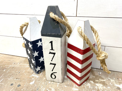 Close-up of decorative 1776 American flag nautical buoy showing hand-painted stars and stripes details, rustic wood texture, and distressed coastal finish