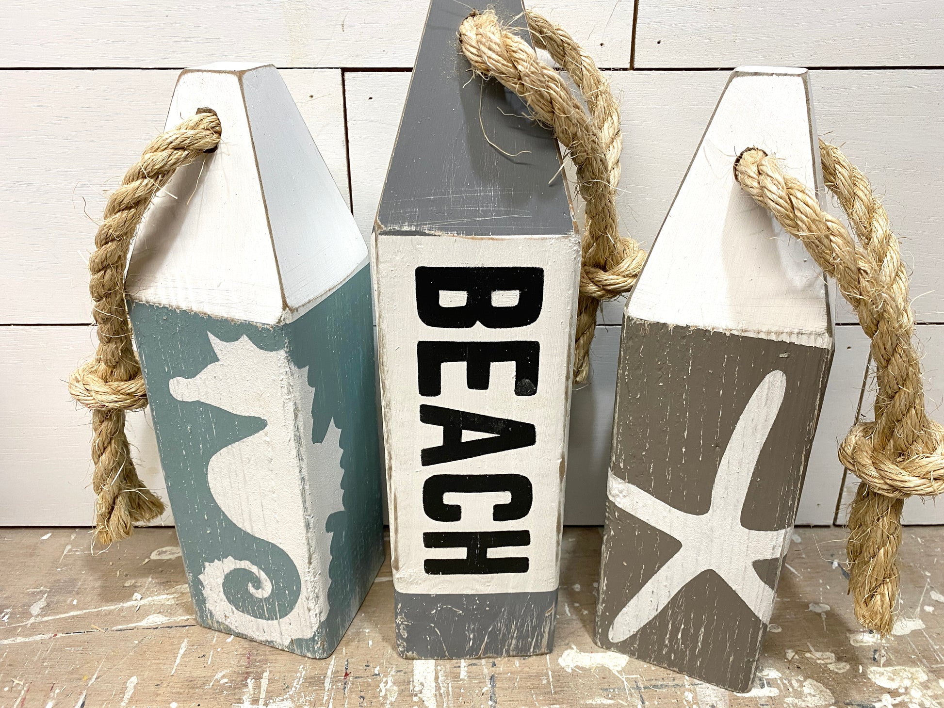 Close-up of beach wood buoy set featuring hand-painted seahorse and starfish designs, distressed wood finish, and rustic nautical details. Coastal decor for beach houses, coastal cottages, beach-themed rooms, ocean-inspired spaces, and seaside homes.