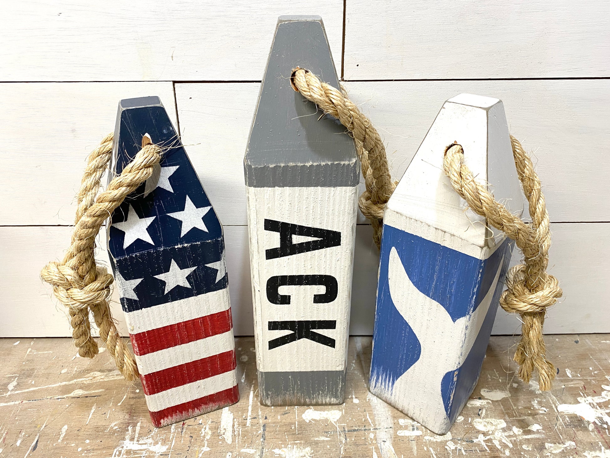 Close-up of decorative Nantucket nautical buoy showing hand-painted ACK lettering, whale tail detail, American flag design, and rustic distressed wood finish
