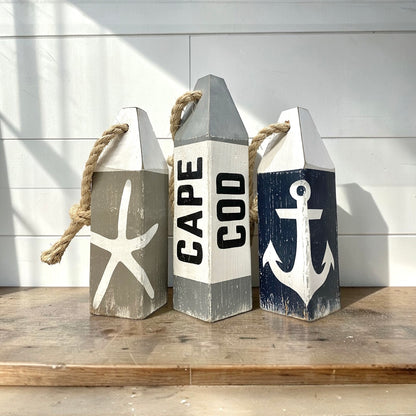 Hand-painted Cape Cod wood buoy set featuring starfish and anchor designs with a distressed finish. Nautical coastal decor for beach houses, coastal cottages, beach-themed rooms, seaside homes, and waterfront spaces.