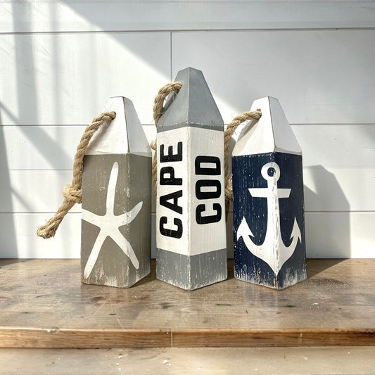Hand-painted Cape Cod wood buoy set featuring starfish and anchor designs with a distressed finish. Nautical coastal decor for beach houses, coastal cottages, beach-themed rooms, seaside homes, and waterfront spaces.