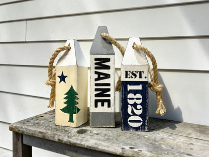 Decorative Maine wood buoy set displayed in a  nautical space. Handmade coastal accents featuring the original Maine flag design, perfect for beach houses, coastal cottages, seaside rooms, harbor-inspired spaces, and New England homes.
