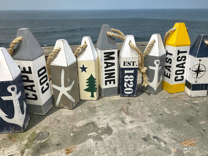 Decorative Maine wood buoy set displayed near the ocean featuring patriotic Maine coastal style. Nautical decor inspired by seaside living, harbors, docks, beach houses, and coastal cottages