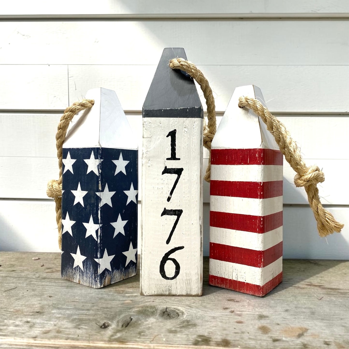 Decorative 1776 American flag wood buoy set featuring patriotic red, white, and blue details with a distressed finish. Nautical Americana decor for beach houses, coastal cottages, patriotic homes, waterfront spaces, and Americana rooms