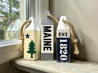 Decorative Maine wood buoy set displayed in a coastal home with nautical decor. Handmade coastal accents featuring the original Maine flag design, perfect for beach houses, coastal cottages, seaside rooms, harbor-inspired spaces, and New England homes.