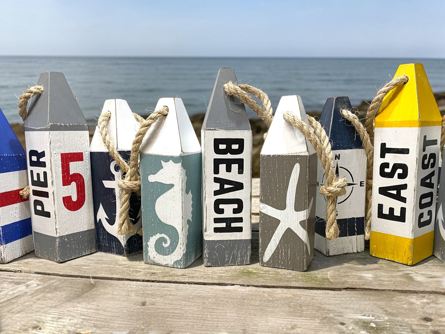 Beach buoy set displayed together near the ocean with seahorse and starfish designs. Nautical coastal decor inspired by beach houses, coastal cottages, seaside living, ocean rooms, and waterfront spaces
