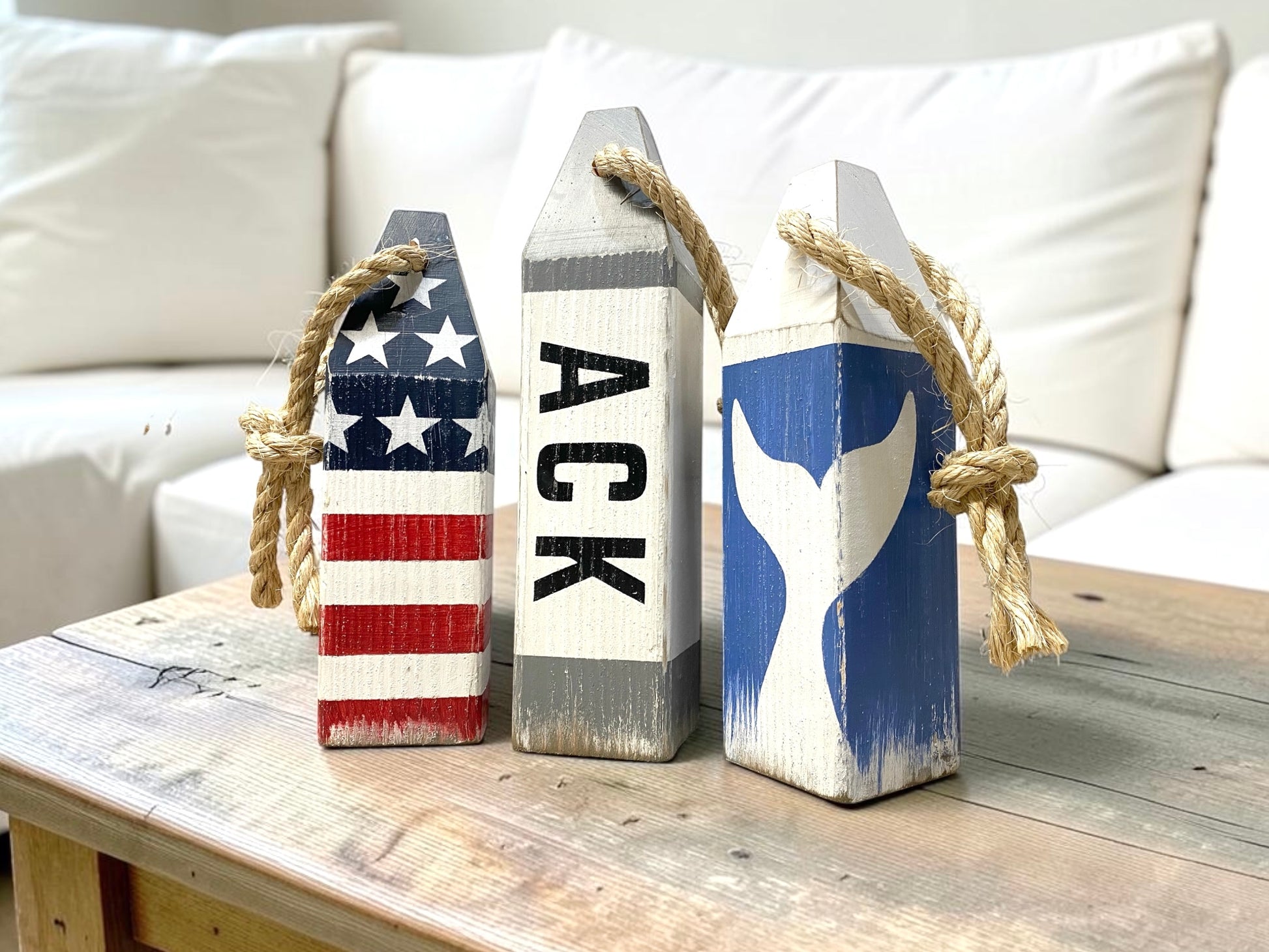 Decorative Nantucket nautical buoy set displayed in a beach living room with coastal decor. Featuring ACK lettering, whale tail, and American flag designs, this handmade wood buoy set adds nautical character to beach houses, seaside cottages, coastal rooms, and ocean-inspired spaces