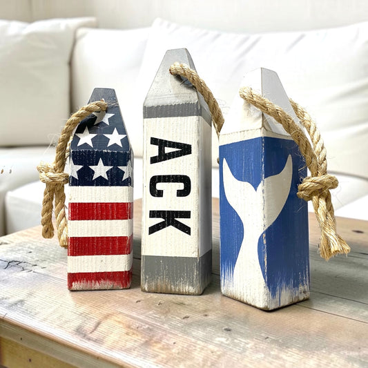 Decorative Nantucket wood buoy set featuring ACK lettering, whale tail design, and patriotic American flag details with a distressed finish. Nautical coastal decor for beach houses, coastal cottages, seaside rooms, waterfront homes, and New England decor