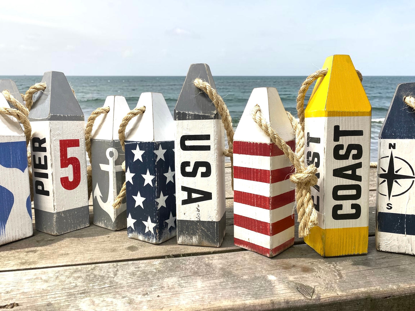 Decorative USA American flag wood buoy set displayed near the ocean with patriotic coastal style. Nautical decor inspired by sailing, boats, harbors, beach houses, and seaside living.