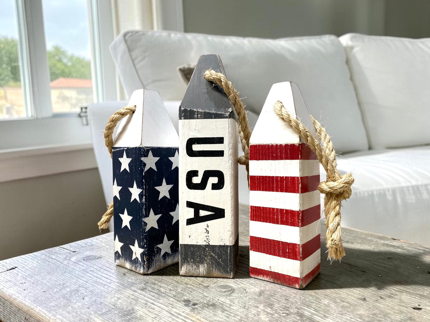 Decorative USA American flag buoy set displayed in an ocean living room with nautical coastal decor. Handmade wood accents featuring patriotic red, white, and blue details, perfect for beach houses, coastal homes, seaside rooms, boating spaces, and Americana decor.