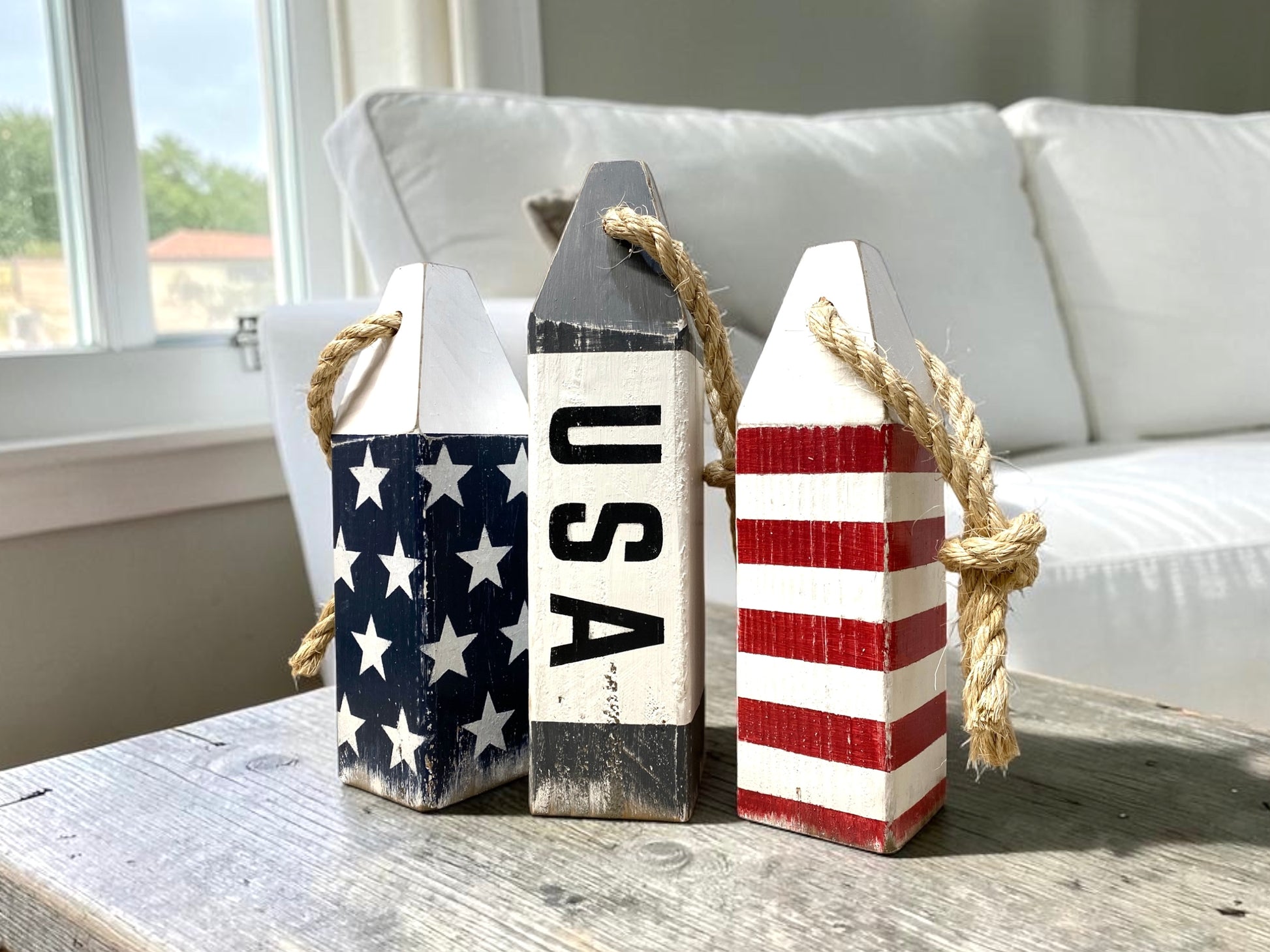 Decorative USA American flag buoy set displayed in an ocean living room with nautical coastal decor. Handmade wood accents featuring patriotic red, white, and blue details, perfect for beach houses, coastal homes, seaside rooms, boating spaces, and Americana decor.
